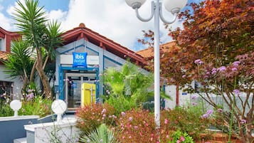 A hotel with a blue and white facade, a visible entrance, and a landscaped garden with various plants and flowers.