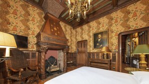 Una stanza con un letto grande, una sedia di legno, un camino e un lampadario.