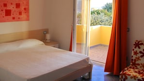 A bedroom with a bed, a nightstand, a chair, a window with curtains, and a view of greenery outside. - Belvedere (Procida)