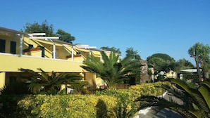 A yellow building with multiple balconies, surrounded by lush greenery and palm trees. - Belvedere (Procida)