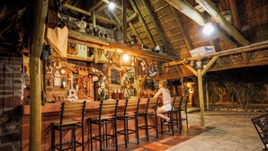 An outdoor bar area with wooden chairs and a stone floor. - Tsauchab River Lodge (Sesriem)