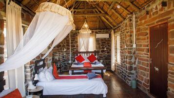 A rustic room with a stone wall, a wooden bed with a canopy, and a stone floor.