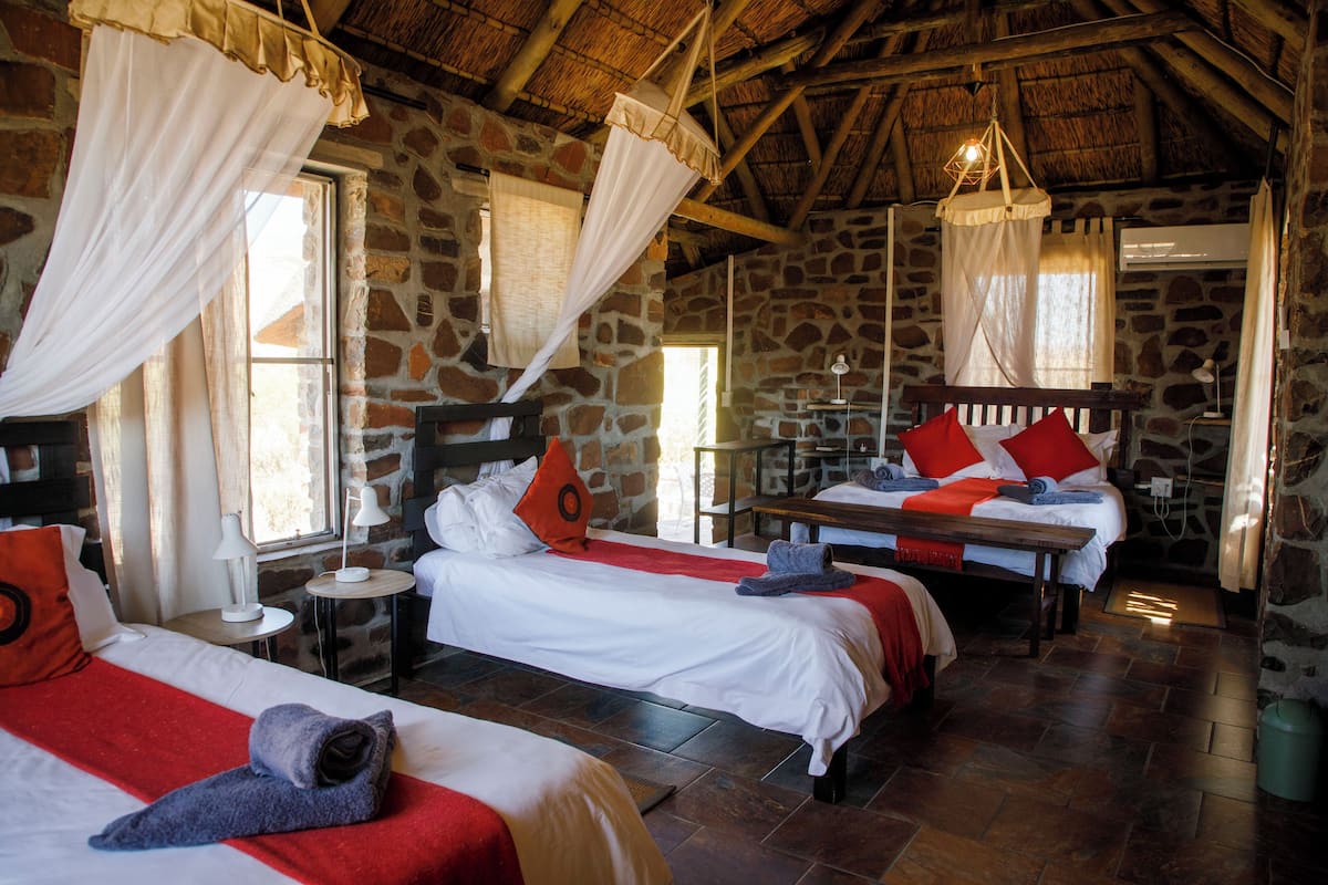 Una habitación con dos camas, paredes de piedra y techo de paja.