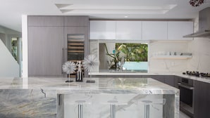 A modern kitchen with marble countertops, stainless steel appliances, and a large island with bar stools. - Modern Del Mar Beach Home (Del Mar)
