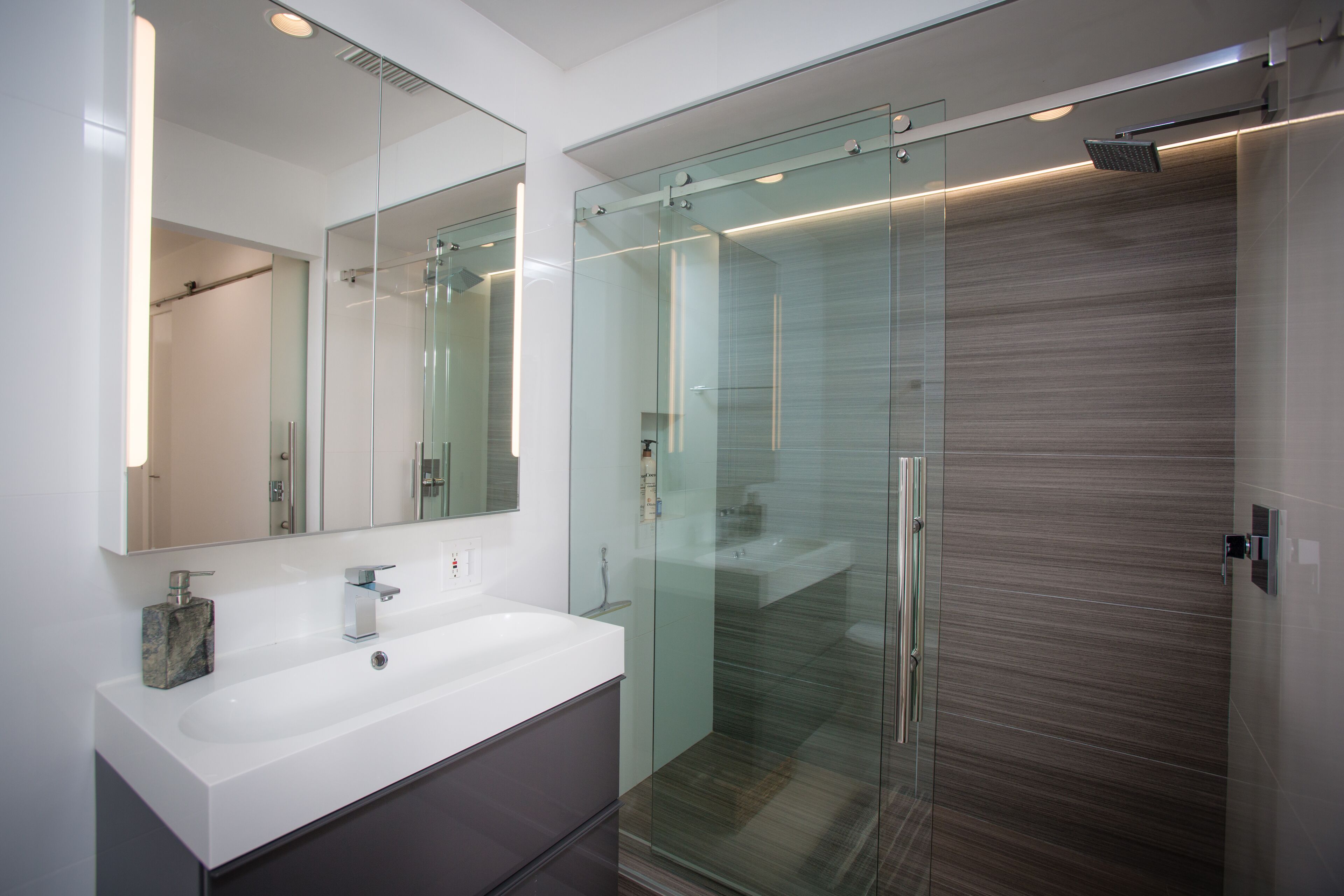 Ein modernes Badezimmer mit einer Glaskabine zur Dusche, einem großen Spiegel und einem Marmorschmuckstück.