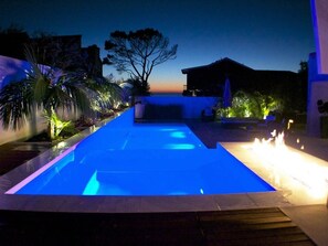A swimming pool with blue lighting, surrounded by palm trees and a building in the background.