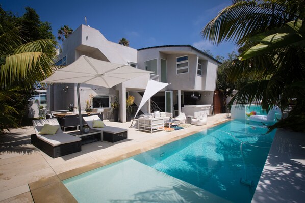 A modern house with a swimming pool, outdoor seating, and palm trees.