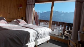 Ein Hotelzimmer mit zwei Betten, einem Balkon mit Bergblick, Holzwänden und einem großen Fenster.