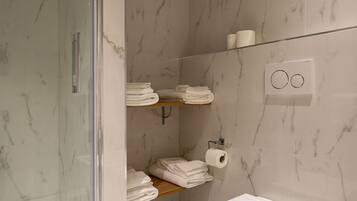A modern bathroom with a glass shower enclosure, marble walls, a toilet, and neatly arranged towels.