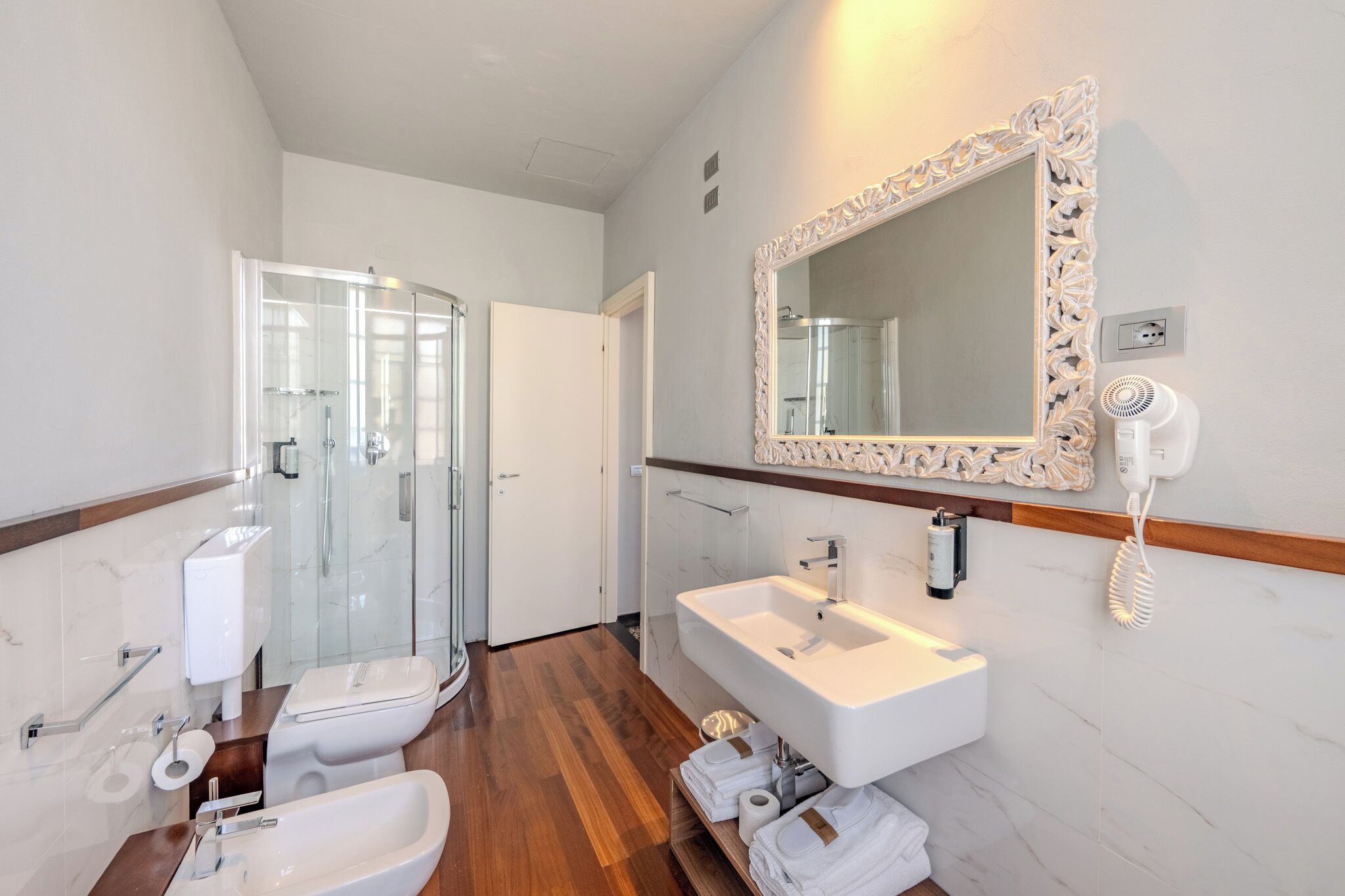Un bagno moderno con cabina doccia in vetro, un water bianco, un lavandino e uno specchio con cornice decorata.