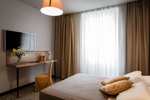 Hotellihuone, jossa on sänky, työpöytä, tuoli, televisio ja ikkuna, jossa on verhot.