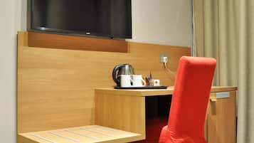 Une chambre d’hôtel avec un bureau en bois, une chaise rouge, un téléviseur à écran plat et une petite table sur laquelle se trouvent une bouilloire et des tasses.