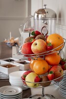 A three-tiered fruit stand with apples, oranges, strawberries, and kiwis.