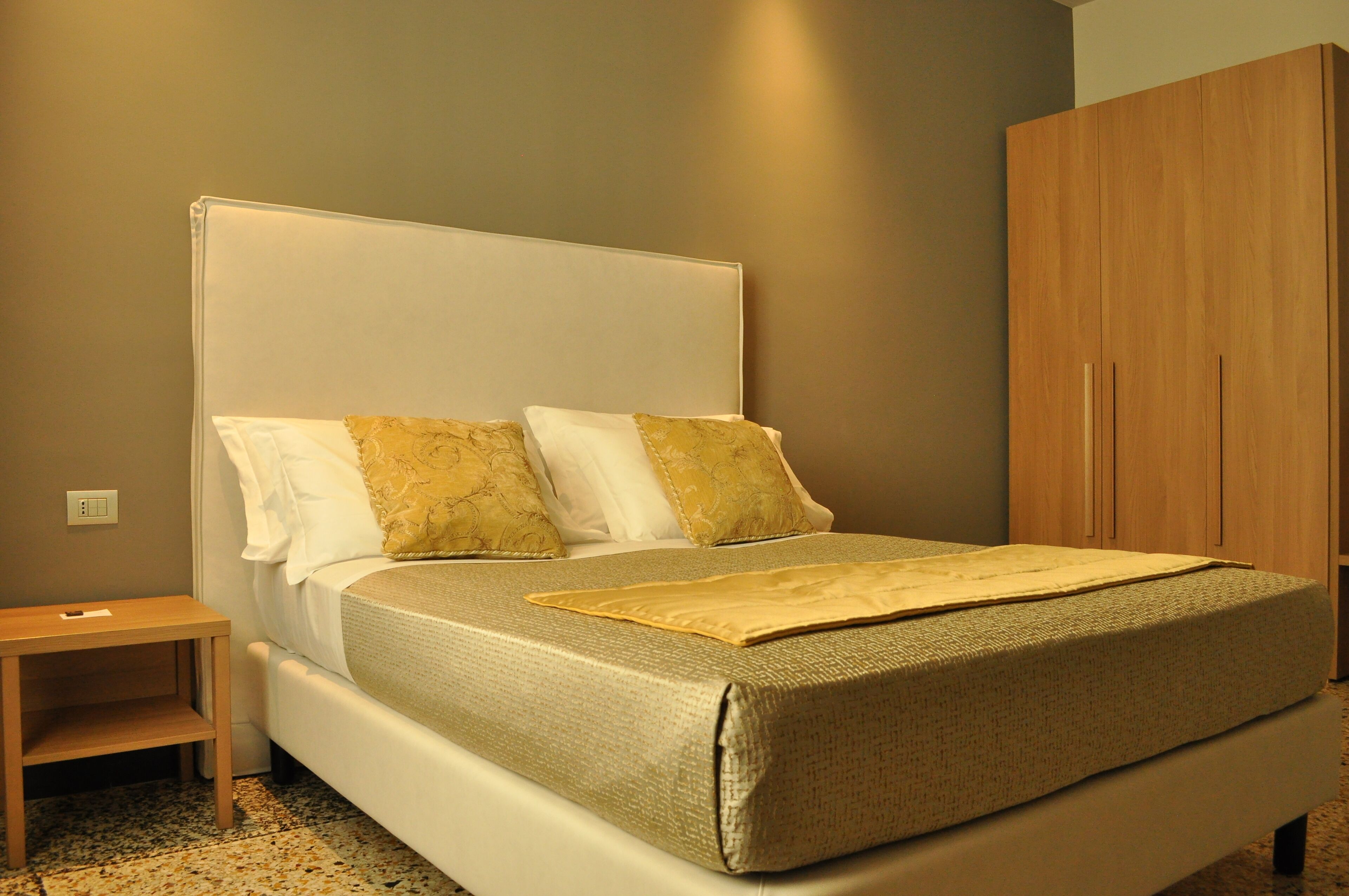 A neatly made bed with a headboard, a wooden nightstand, and a wardrobe.