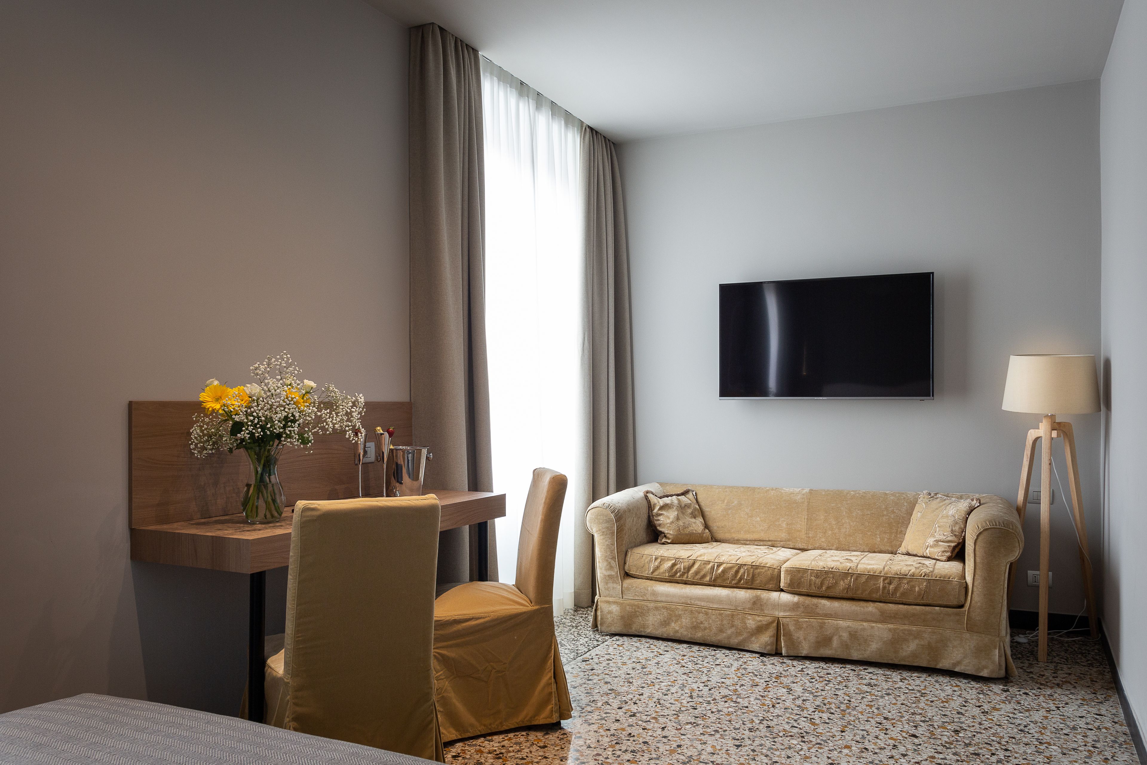 Habitación de hotel con cama, sofá, escritorio con un florero y televisión, además de una lámpara.