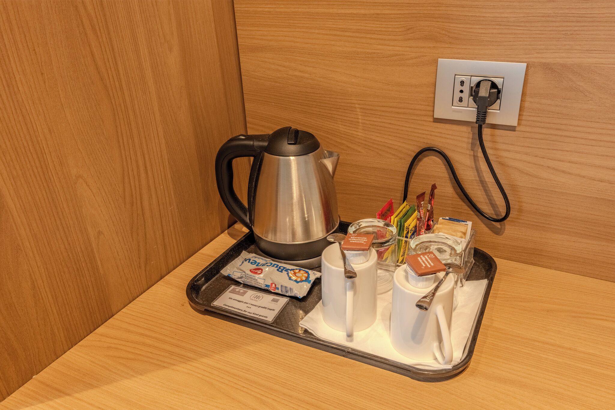 Una bandeja con tetera, tazas y refrigerios empaquetados sobre una superficie de madera.