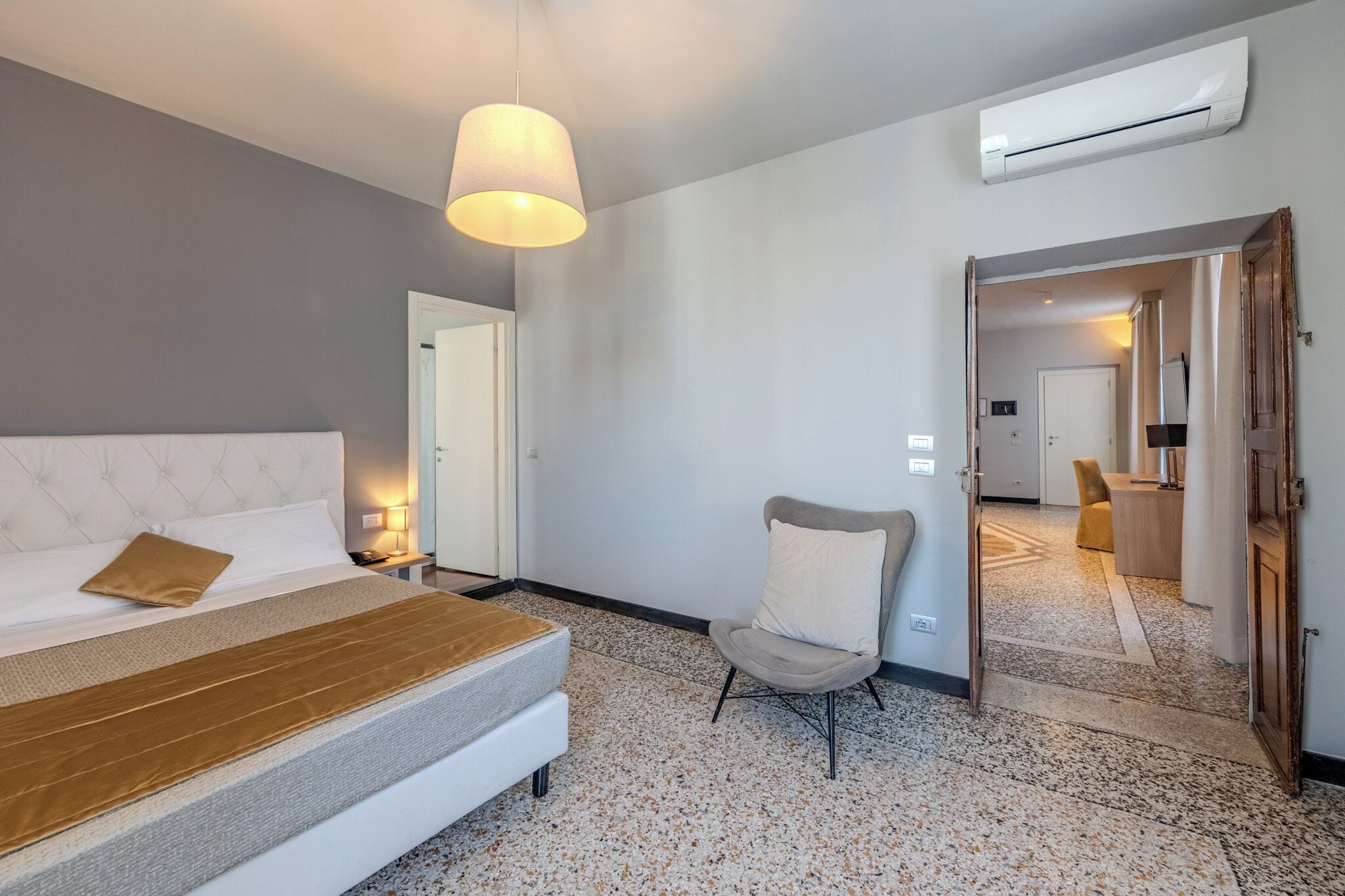 Une chambre d’hôtel comprenant un lit, une chaise, un appareil de climatisation et une porte donnant sur une autre pièce.