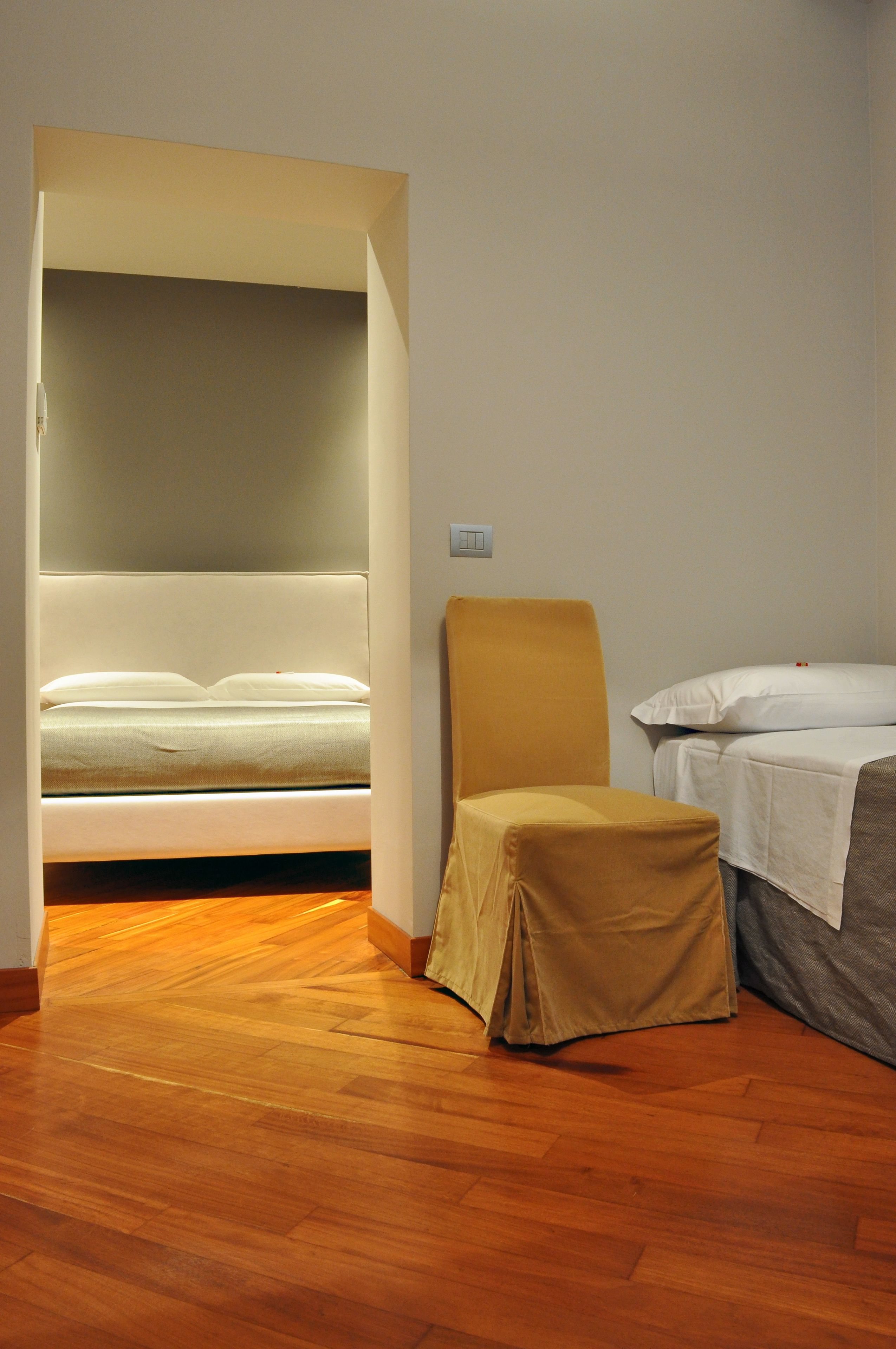 Una stanza con un letto, una sedia e un pavimento in legno.