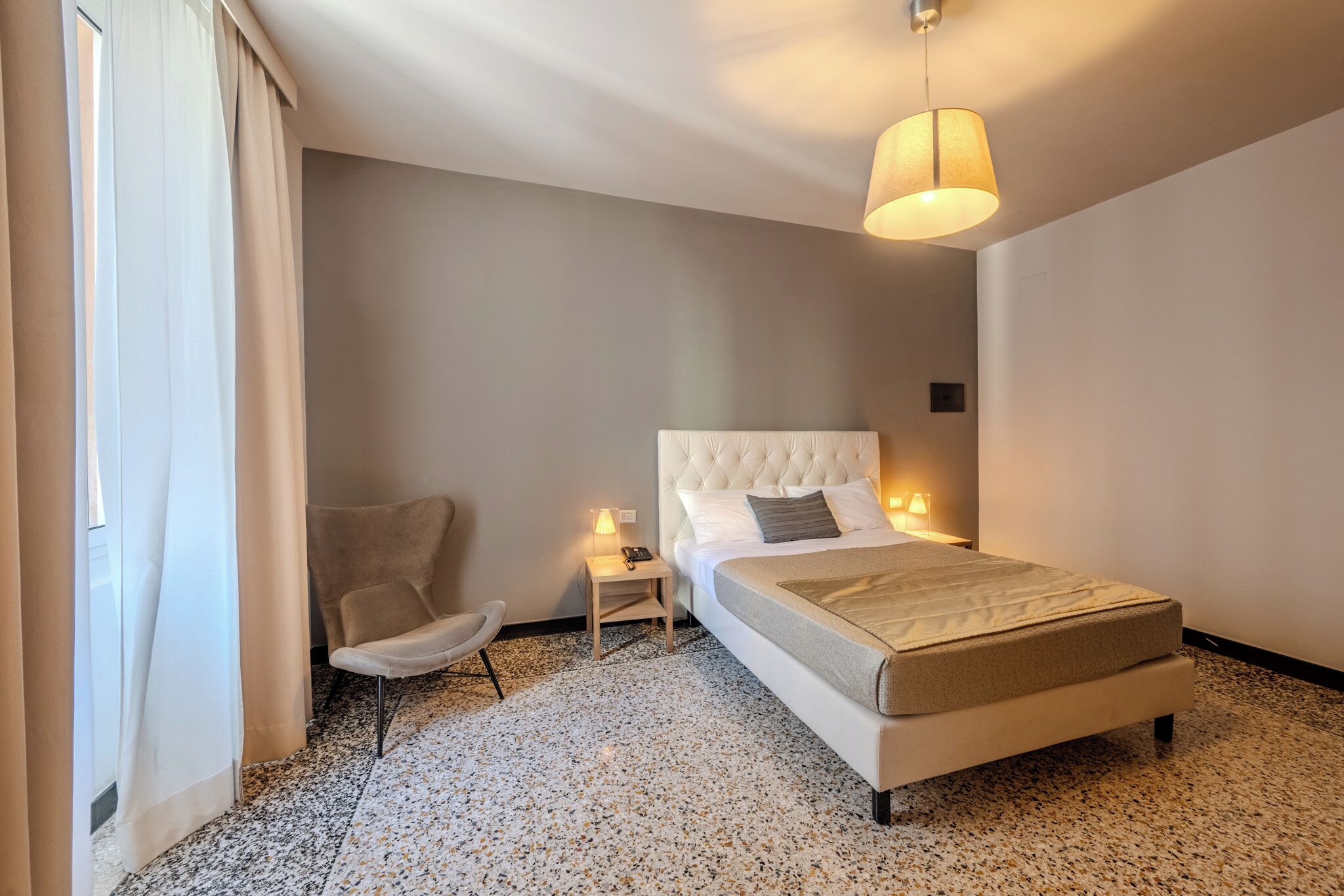 A hotel room with a bed, a chair, a nightstand, and a lamp.