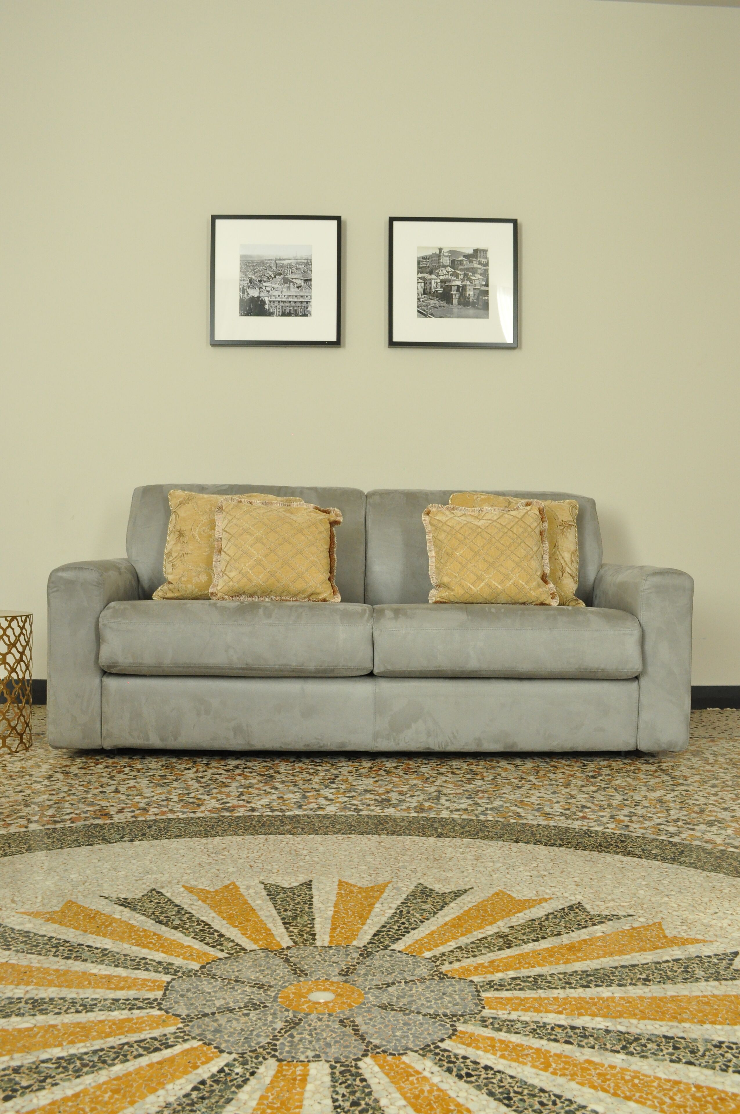 A grey sofa with two decorative pillows, a framed black and white photograph on the wall, and a patterned floor.