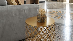 Una sala de estar moderna con un sofá gris, estanterías de madera, una mesa de centro redonda con objetos decorativos y una lámpara colgante.