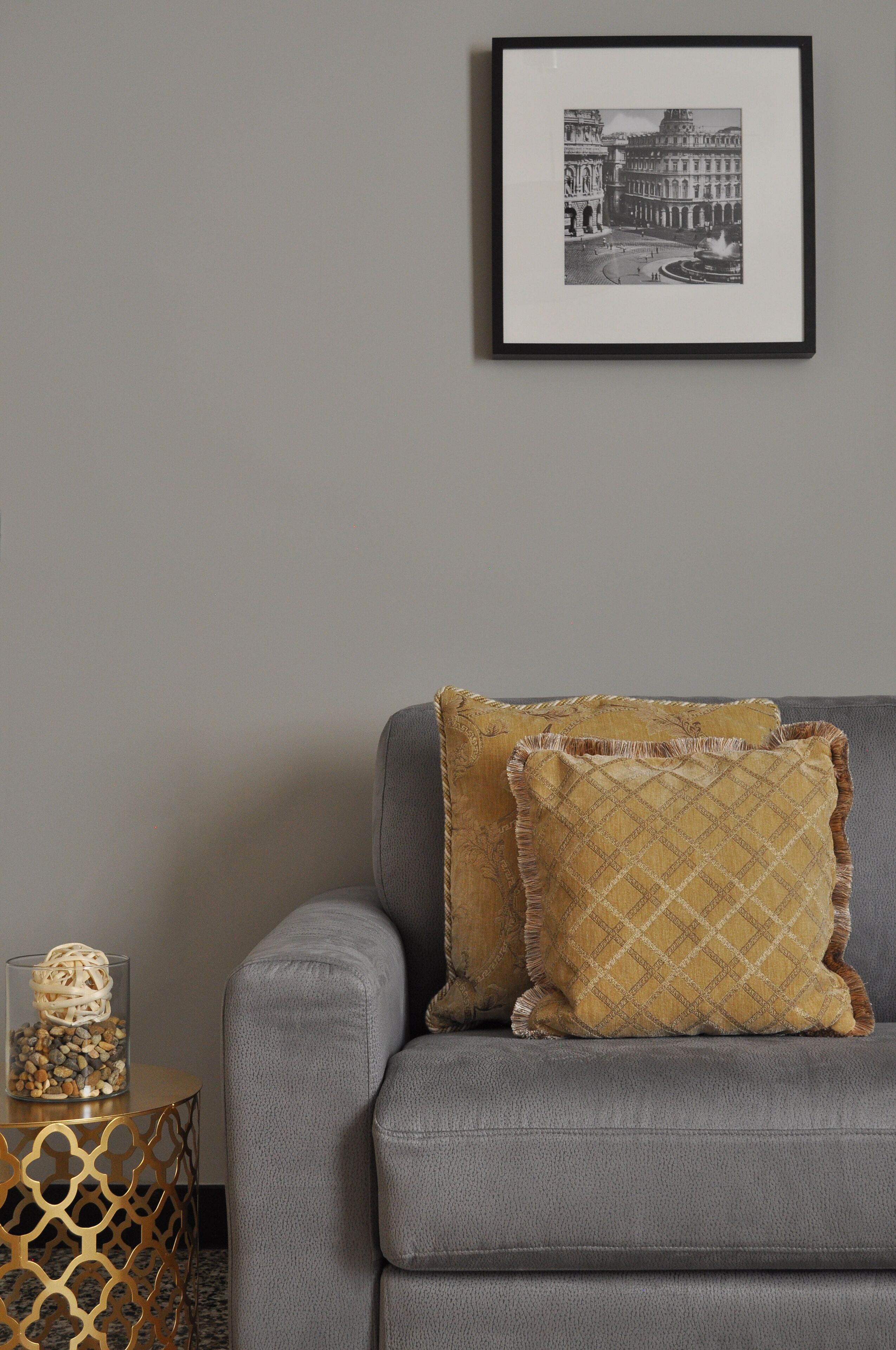 Un canapé gris agrémenté de coussins à motifs, un tableau encadré accroché au mur et une table d’appoint sur laquelle se trouve un récipient en verre.