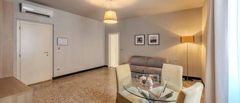 Une chambre d’hôtel équipée d’une kitchenette, d’un canapé, d’une table à manger en verre avec des chaises et d’un luminaire au plafond.