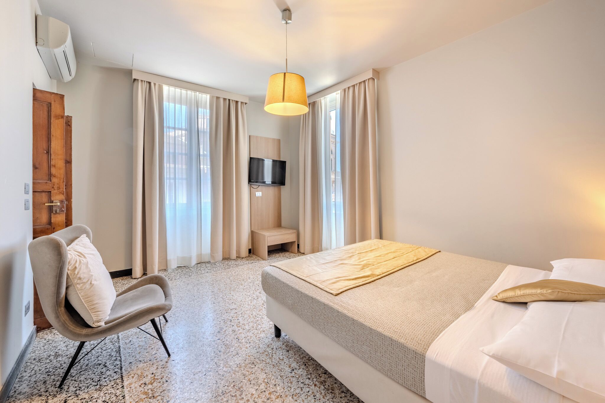 Une chambre d’hôtel avec un lit, une chaise, une télévision et une fenêtre avec des rideaux.