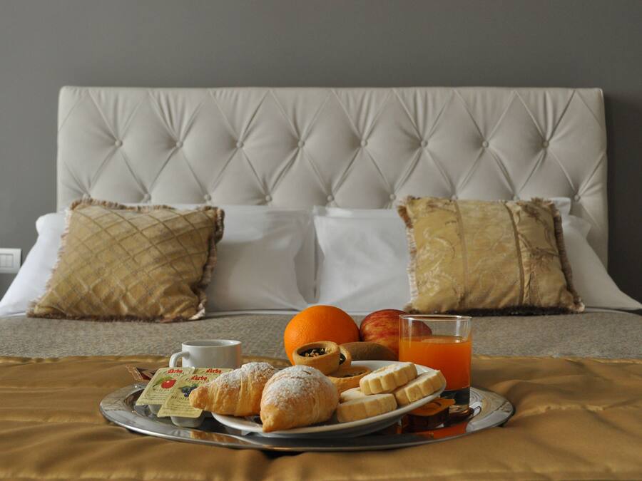 A neatly made bed with a tufted headboard, two pillows, a tray with croissants, a plate with fruit, a glass of orange juice, and a cup of coffee.