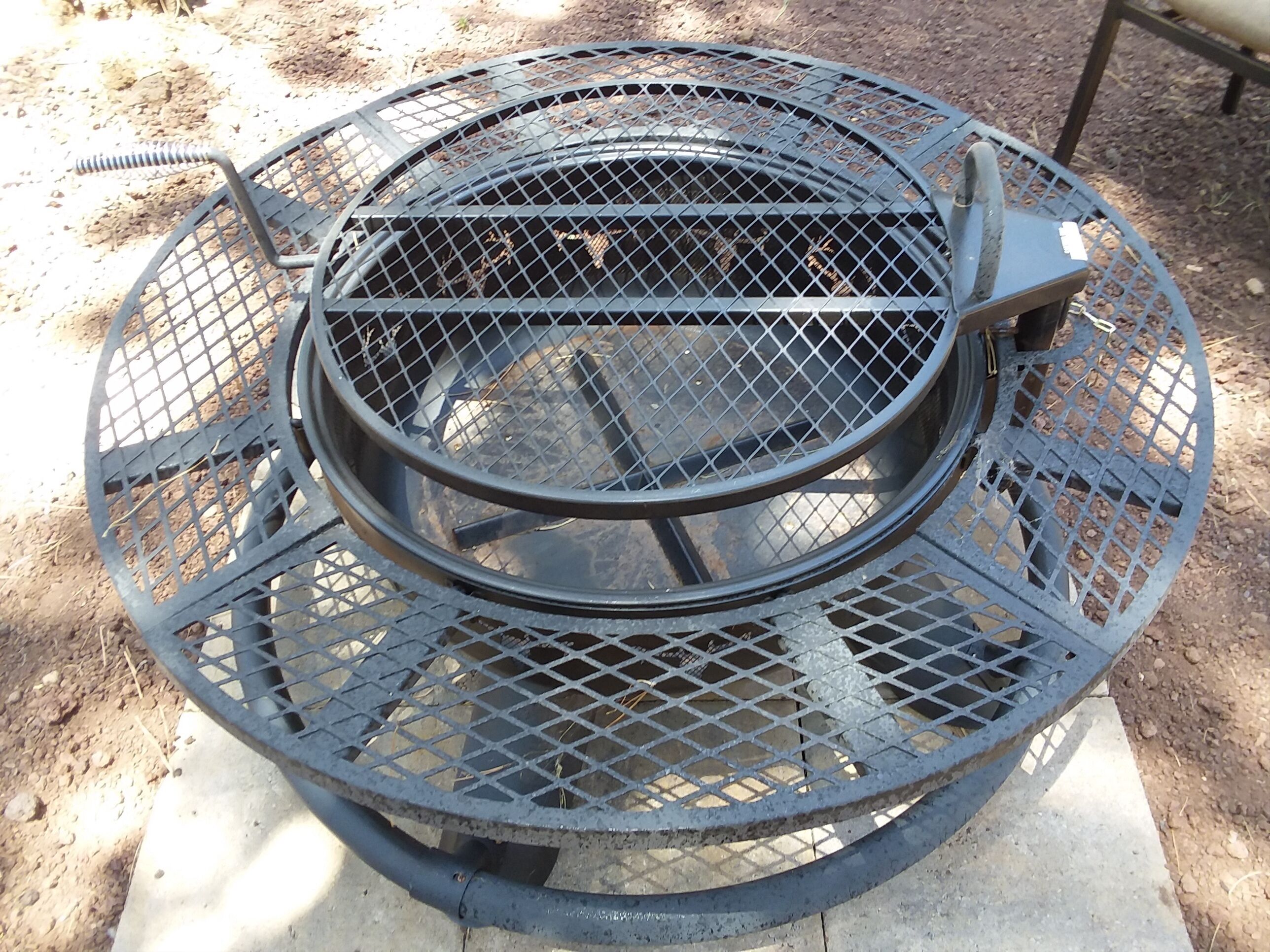 Un gril en métal, de forme circulaire et doté d’une cheminée centrale, installé sur une base en béton à l’extérieur.