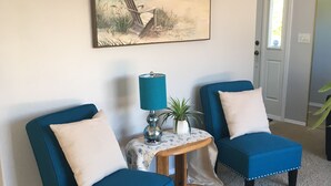 A room with two blue armchairs, a small table with a lamp, a painting of a beach scene, and a door with a window. - 3 Bedroom Haven By The Sea w/ beautiful ocean views & 2 Masters Sleeps 10 (Lincoln City)