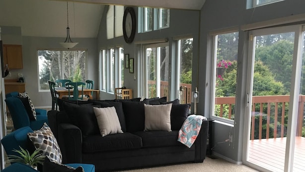 A spacious living room with a large black sofa, teal armchairs, and a carpeted floor. - 3 Bedroom Haven By The Sea w/ beautiful ocean views & 2 Masters Sleeps 10 (Lincoln City)