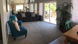 A spacious living room with a dark-colored sofa, teal armchairs, and a wooden dining table. - 3 Bedroom Haven By The Sea w/ beautiful ocean views & 2 Masters Sleeps 10 (Lincoln City)