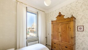 Une chambre avec deux lits, une armoire en bois, une fenêtre avec des rideaux et une vue sur un immeuble.
