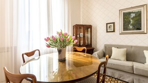 Un coin repas comprenant une table ronde en verre, des chaises en bois, un vase de fleurs, un buffet en bois et un canapé.