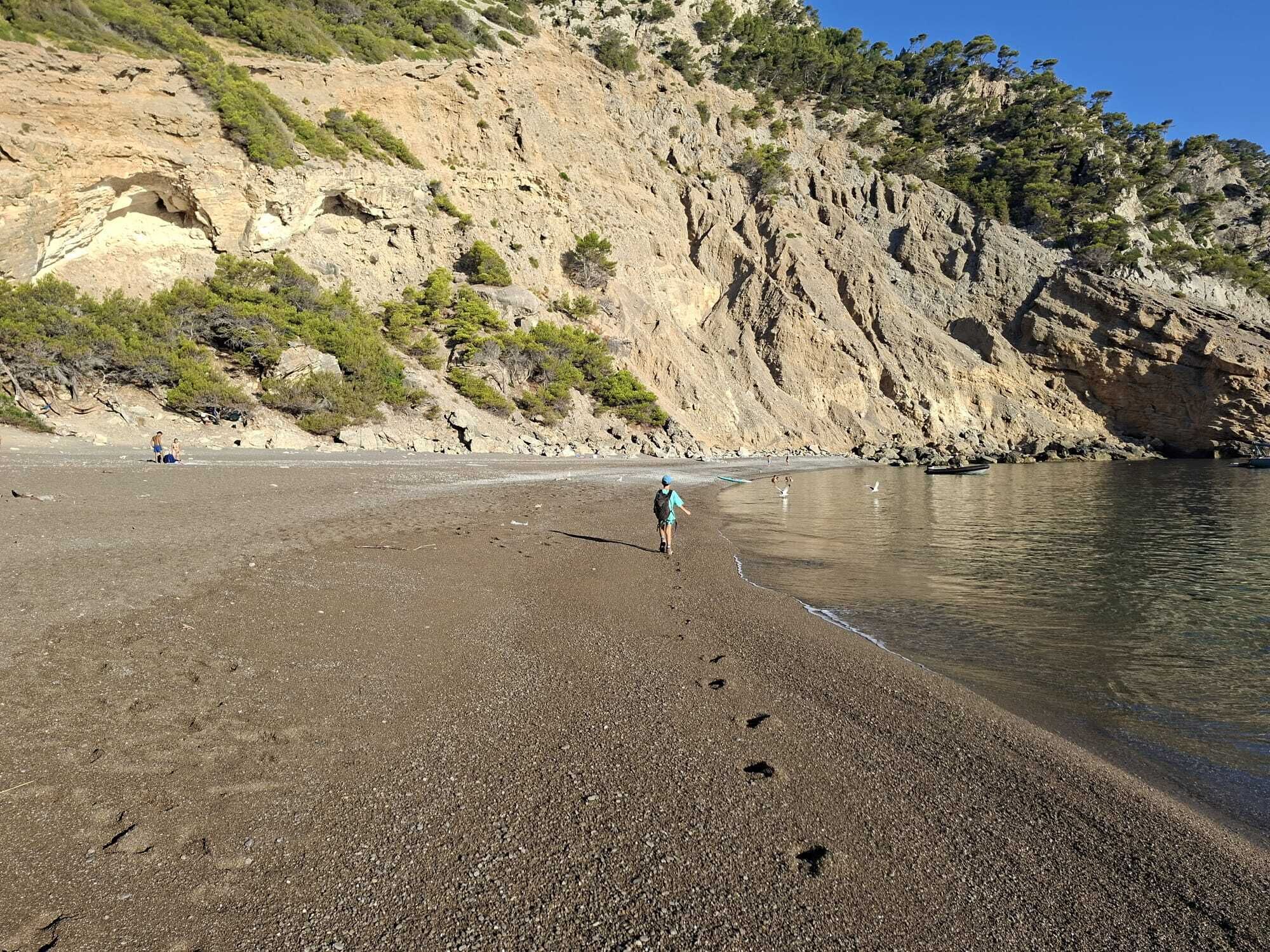 Une plage de galets bordée de falaises rocheuses et où la végétation est clairsemée.