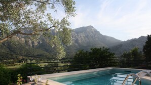 Une piscine avec vue sur les montagnes, une table avec une bouteille et des verres, et une chaise avec une serviette rouge.
