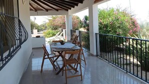 Eine überdachte Terrasse im Freien mit Tisch und Stühlen, umgeben von einem Metallgeländer und Blick ins Grüne.