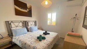 Een slaapkamer met een bed, een bankje, een raam en een schilderij aan de muur.