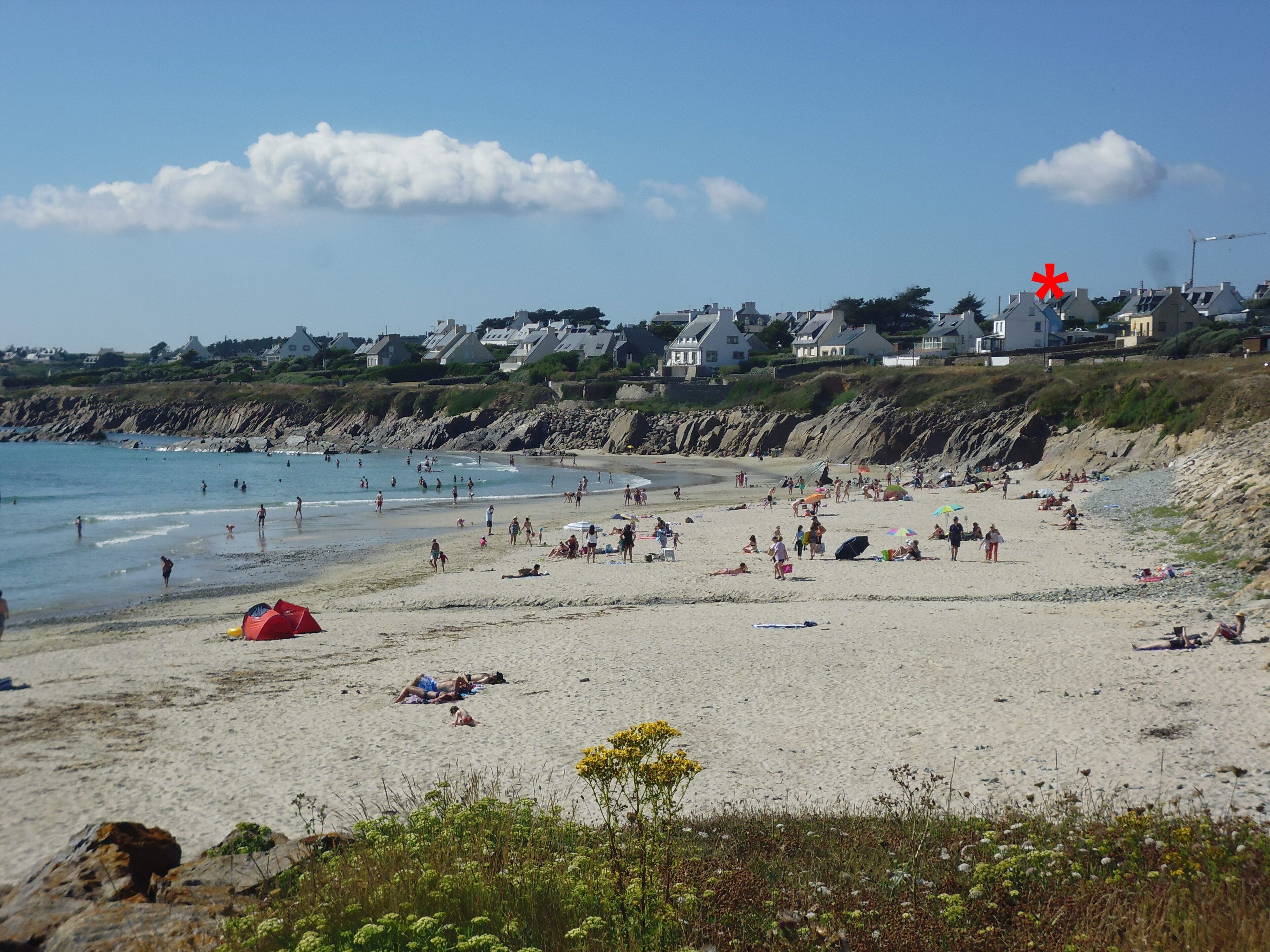 A beach with people, tents, and houses in the background.