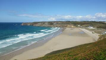 A coastal beach with a sandy shore, a rocky cliff, and a few buildings in the distance.