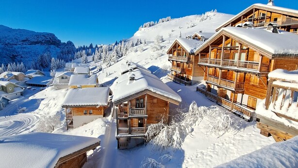 A snow-covered mountain resort with wooden buildings, including a large lodge with balconies and a smaller cabin. - Beautiful apartment/duplex in the Savoyard style in a spectacular setting (Arâches-La-Frasse)