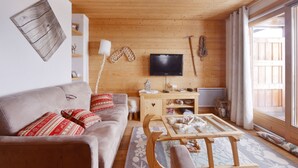 A cozy living room with a wooden ceiling, a sofa with red cushions, a TV, and a wooden cabinet. - Beautiful apartment/duplex in the Savoyard style in a spectacular setting (Arâches-La-Frasse)