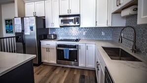 A modern kitchen with white cabinets, a stainless steel refrigerator, a microwave, an oven, and a sink.