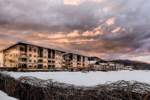 A multi-story hotel with balconies, a snow-covered landscape, and mountains in the background.