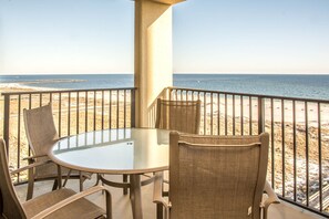 Een balkon met een glazen tafel en rieten stoelen, met uitzicht op een strand en helder zicht op de oceaan.