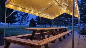 A wooden picnic table under a canopy with string lights. - Huge Indiana Family Reunion Villa with Indoor Pool, Hot Tub, Game Rm 8 BR, 7 BA (Winchester)