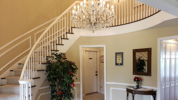 A grand staircase with a chandelier, a potted plant, and a framed picture on the wall. - Huge Indiana Family Reunion Villa with Indoor Pool, Hot Tub, Game Rm 8 BR, 7 BA (Winchester)