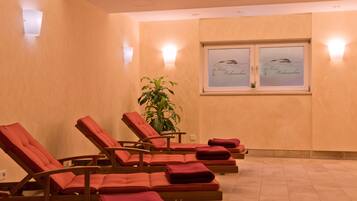 Relax in a serene spa room with comfortable lounge chairs, framed artworks, and a potted plant.
