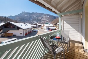 Un balcon avec une table et des chaises, donnant sur une rue bordée d’immeubles et avec une montagne en arrière-plan.
